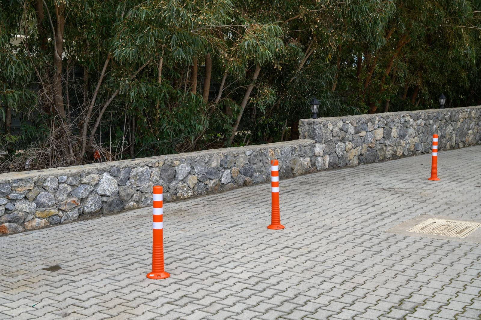 Orange traffic cones form a clear boundary in a tranquil parking area surrounded by lush greenery and a stone wall.