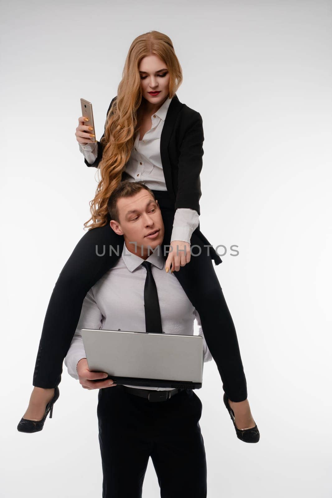 A couple shows a fun dynamic, with the woman playfully on the man's shoulders as he works on his laptop.