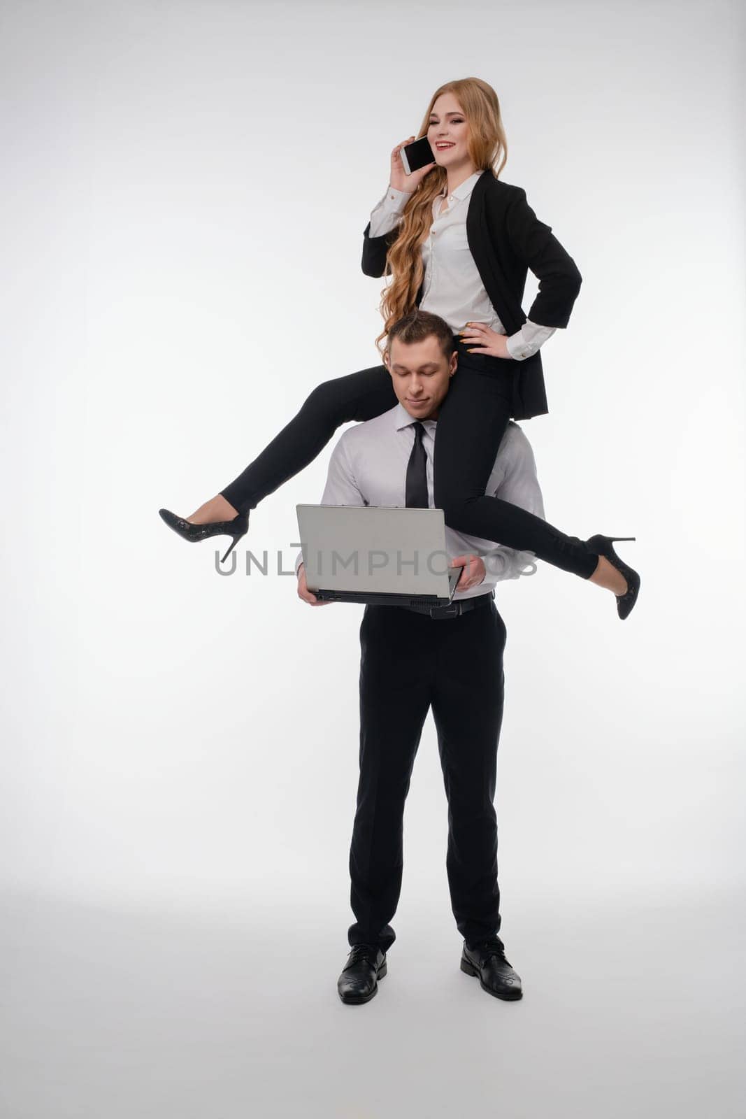 A couple enjoys a fun activity, with one balancing on the other's shoulders while using a laptop.
