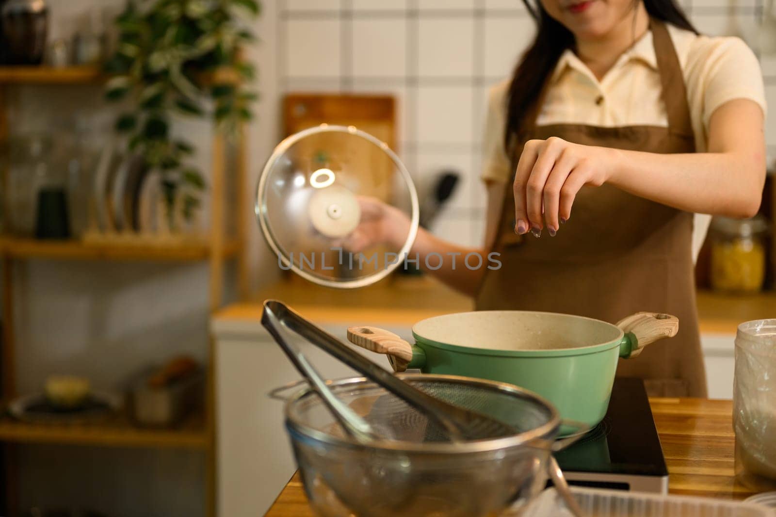 Shot of woman sprinkles seasoning into a simmering pan of tomato based spaghetti sauce..