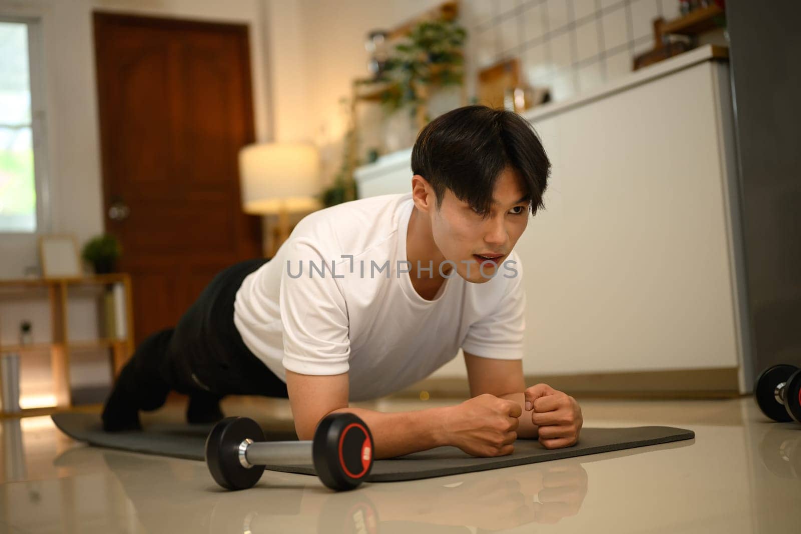Young Asian man doing plank exercise on yoga mat at home.