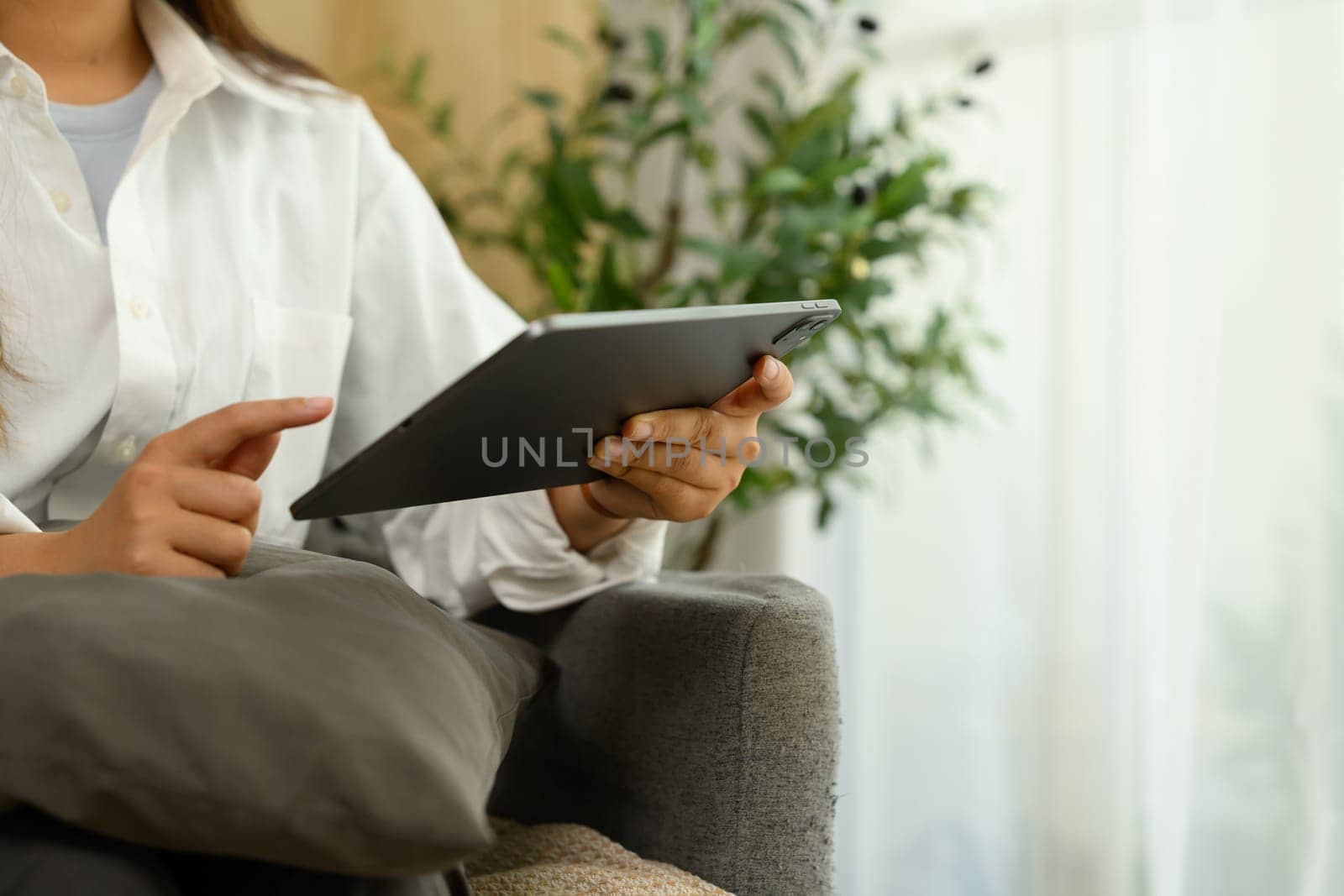 Cropped shot of female freelancer using a digital tablet while sitting on a comfortable couch.