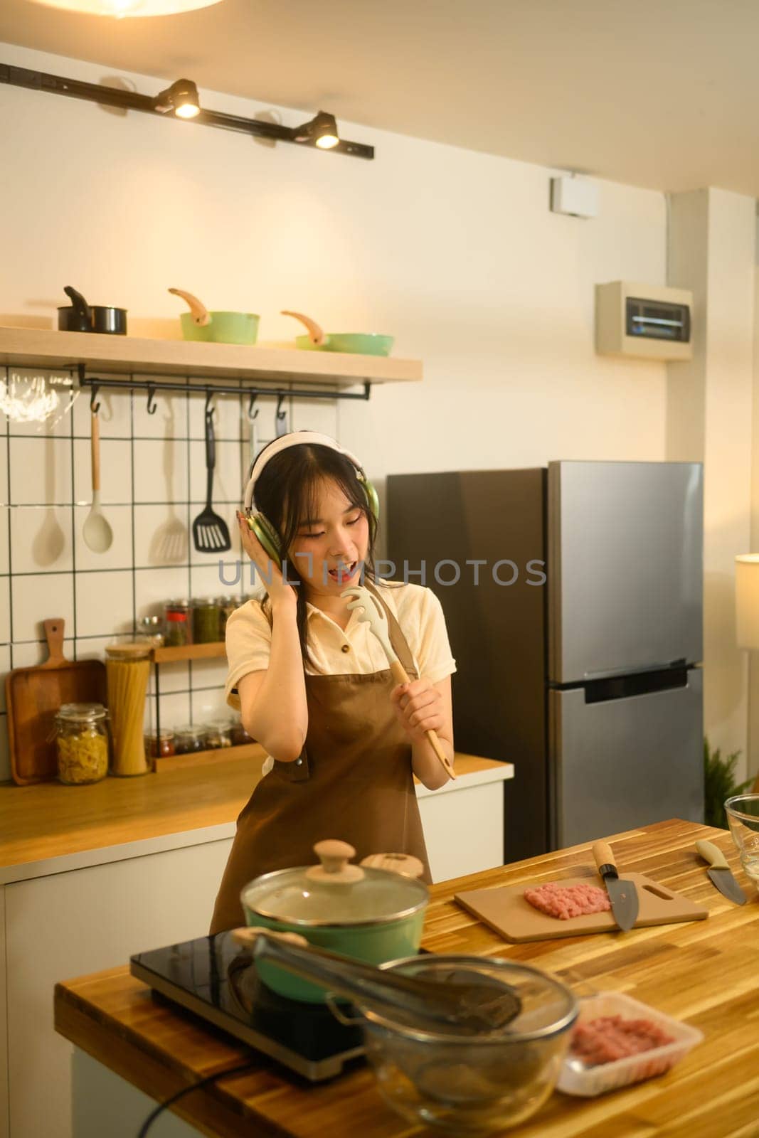 Happy young woman listening to music while preparing a homemade spaghetti in a kitchen.
