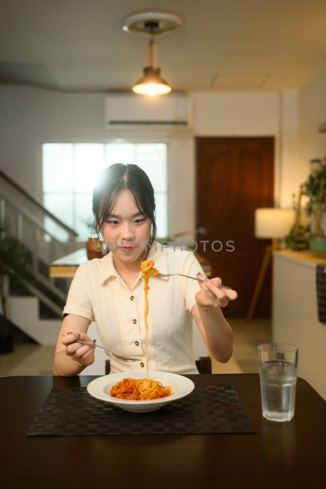 Asian woman enjoying a homemade spaghetti at a dining table.