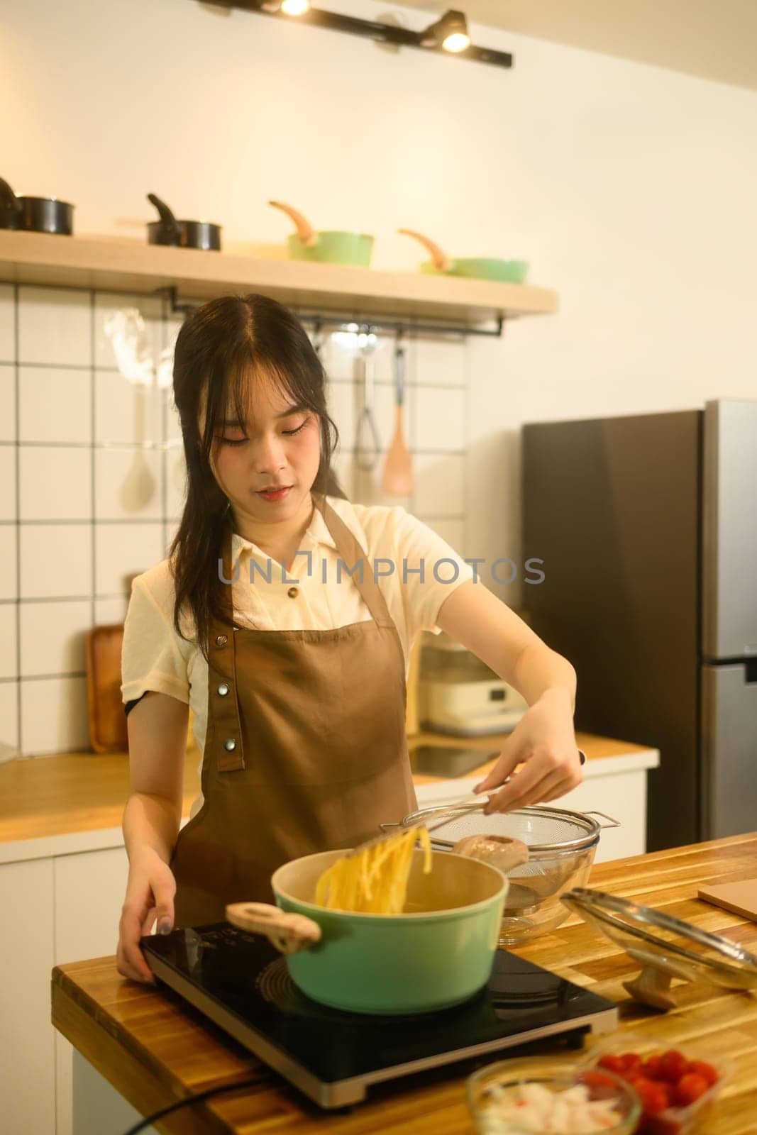 Smiling woman lifting boiled spaghetti from steaming pot while preparing a delicious homemade dish.