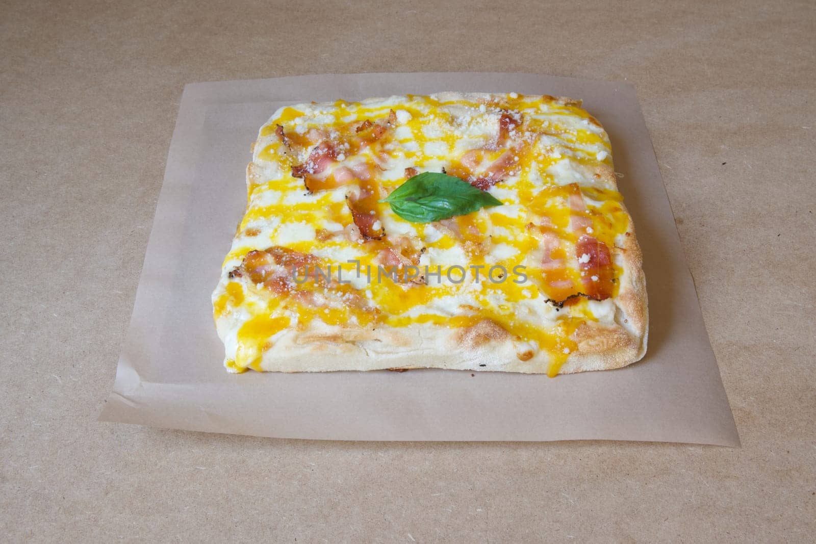A slice of pizza with bacon and cheese on top. The pizza is sitting on a brown paper