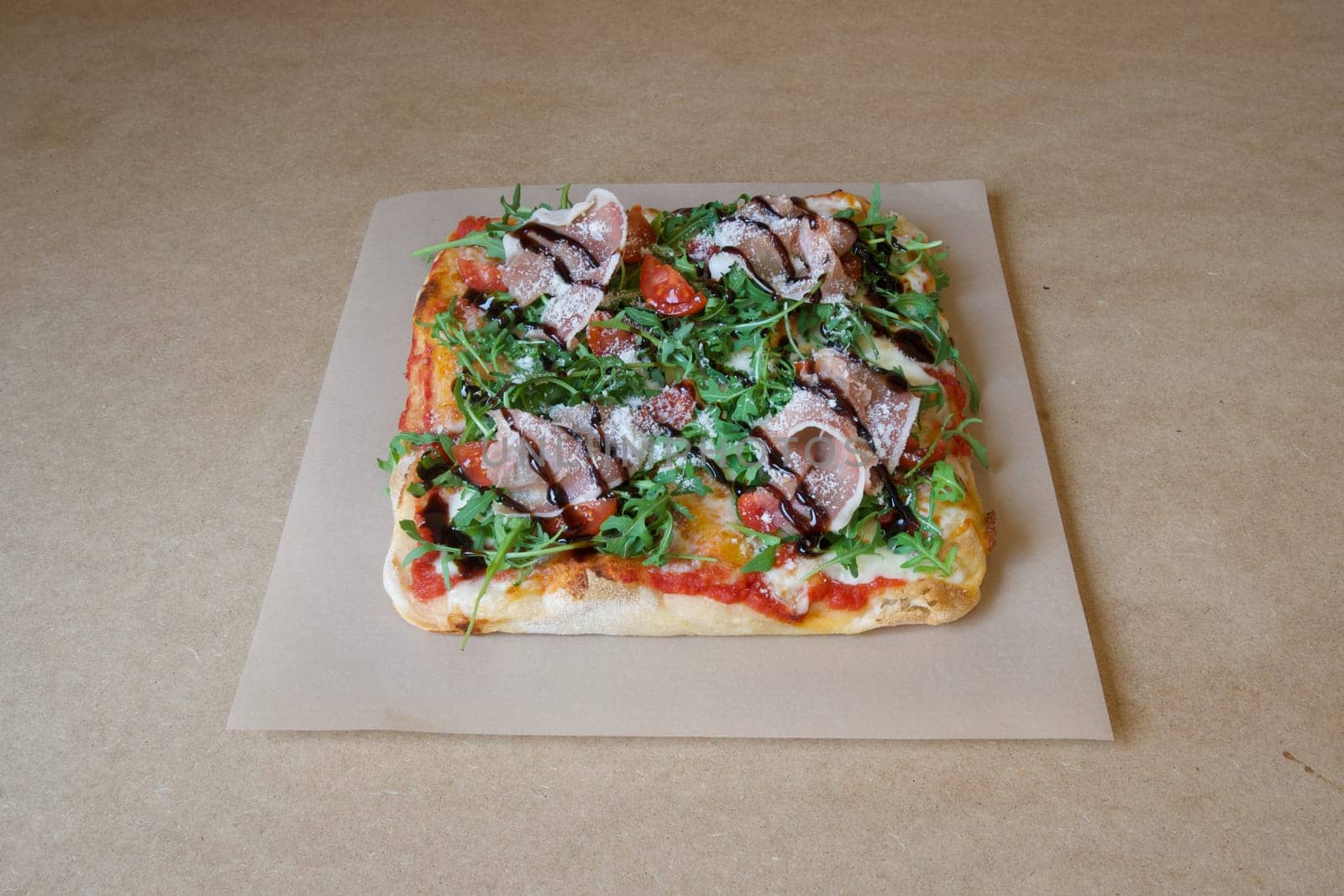 A pizza with basil and tomatoes on it. The pizza is on a brown paper