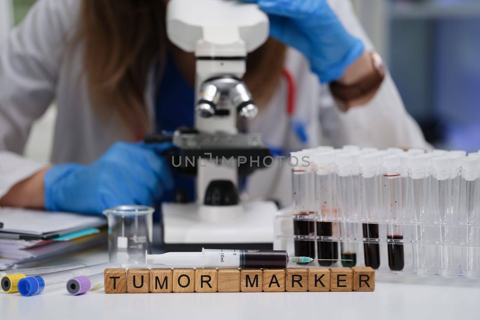 A scientist is meticulously examining tumor markers in a laboratory using test tubes and a microscope setup