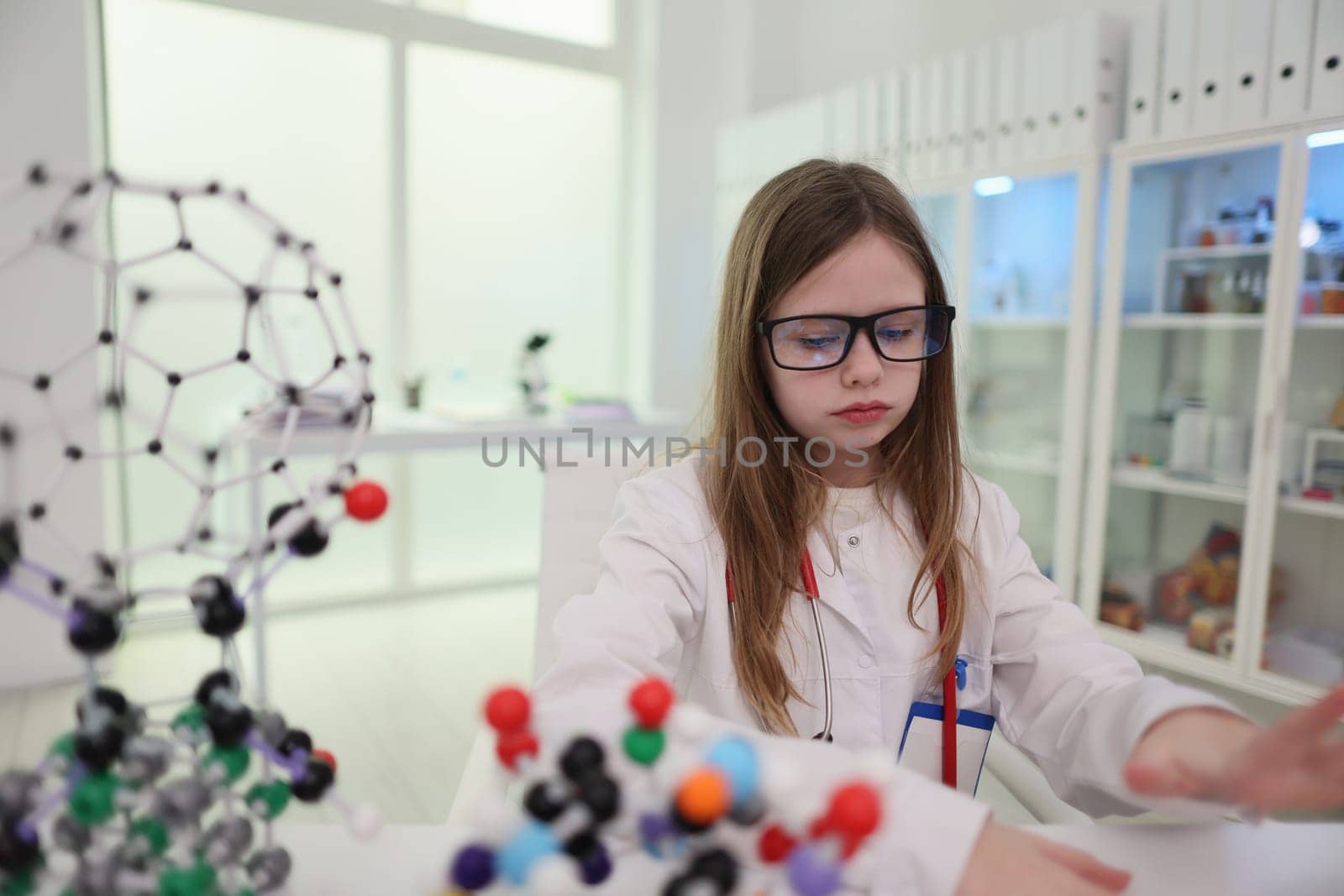A young girl scientist, dressed in a lab coat, diligently works with intricate molecular models in her lab