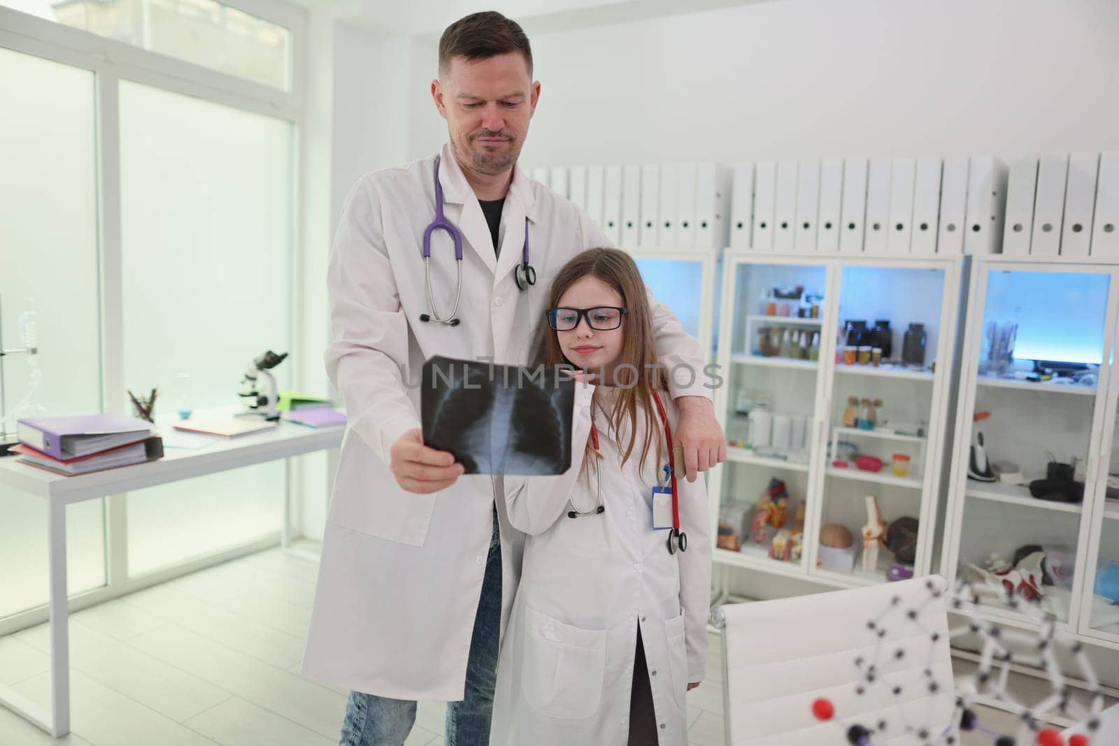 In a bright and cheerful medical setting, a doctor and a young girl wearing lab coats are examining an Xray