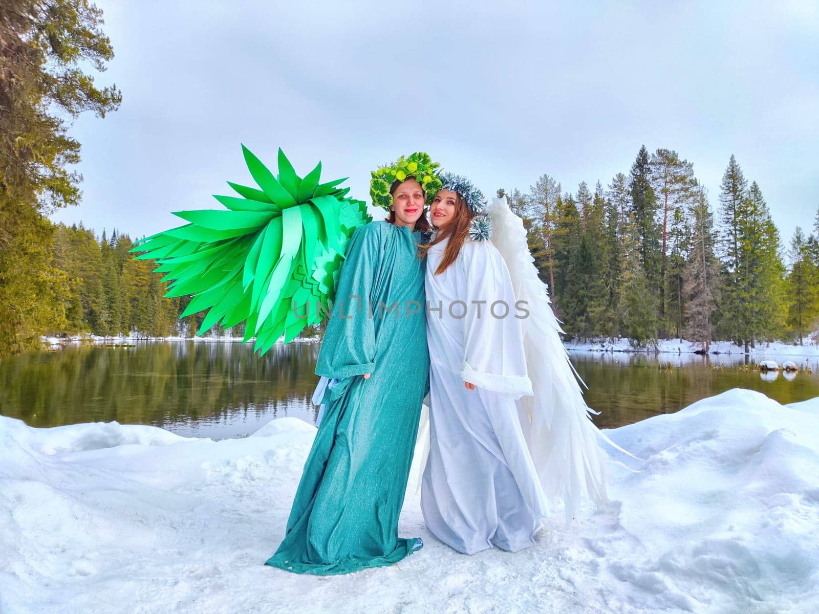 Two girls in white and green attire pose at a lake, symbolizing the shift from winter to spring in nature.