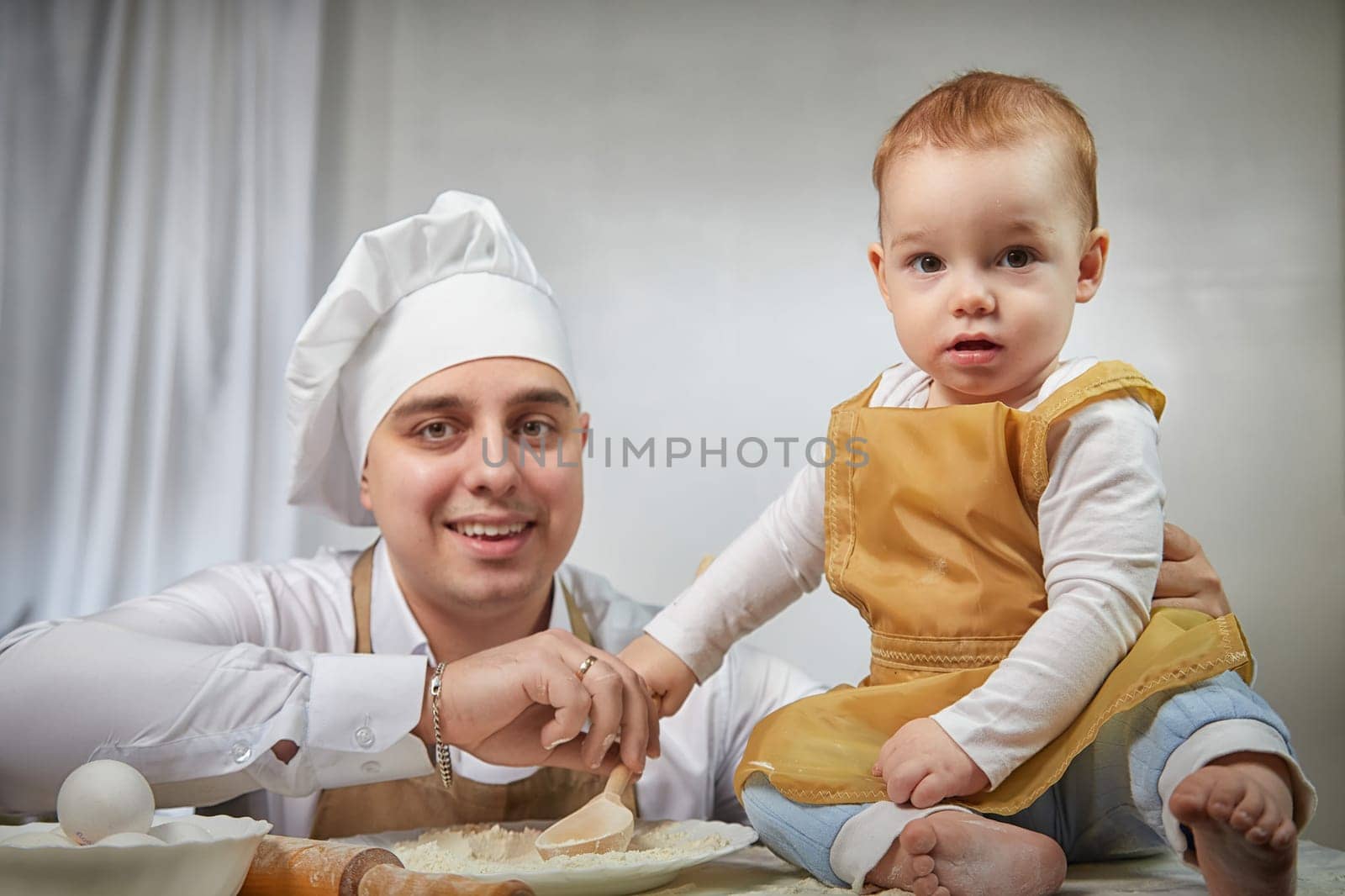 A family enjoys a fun cooking session, playfully covered in flour while engaging with their little ones in a warm kitchen. Father and son having fun