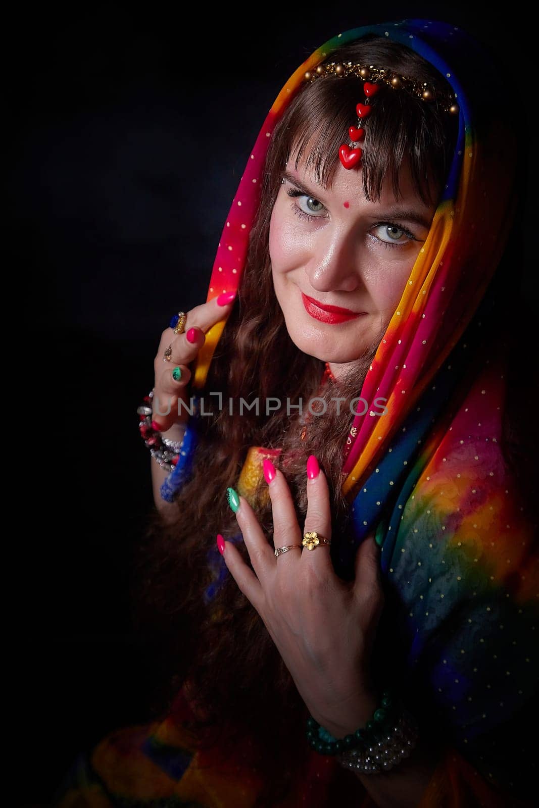 A mature woman with long hair styled beautifully poses in a colorful sari and dupatta, embracing Indian culture in a creative setting.
