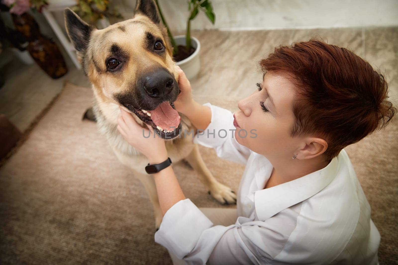 Blonde woman interacts lovingly with her German Shepherd dog in a comfortable home environment, capturing a warm moment.