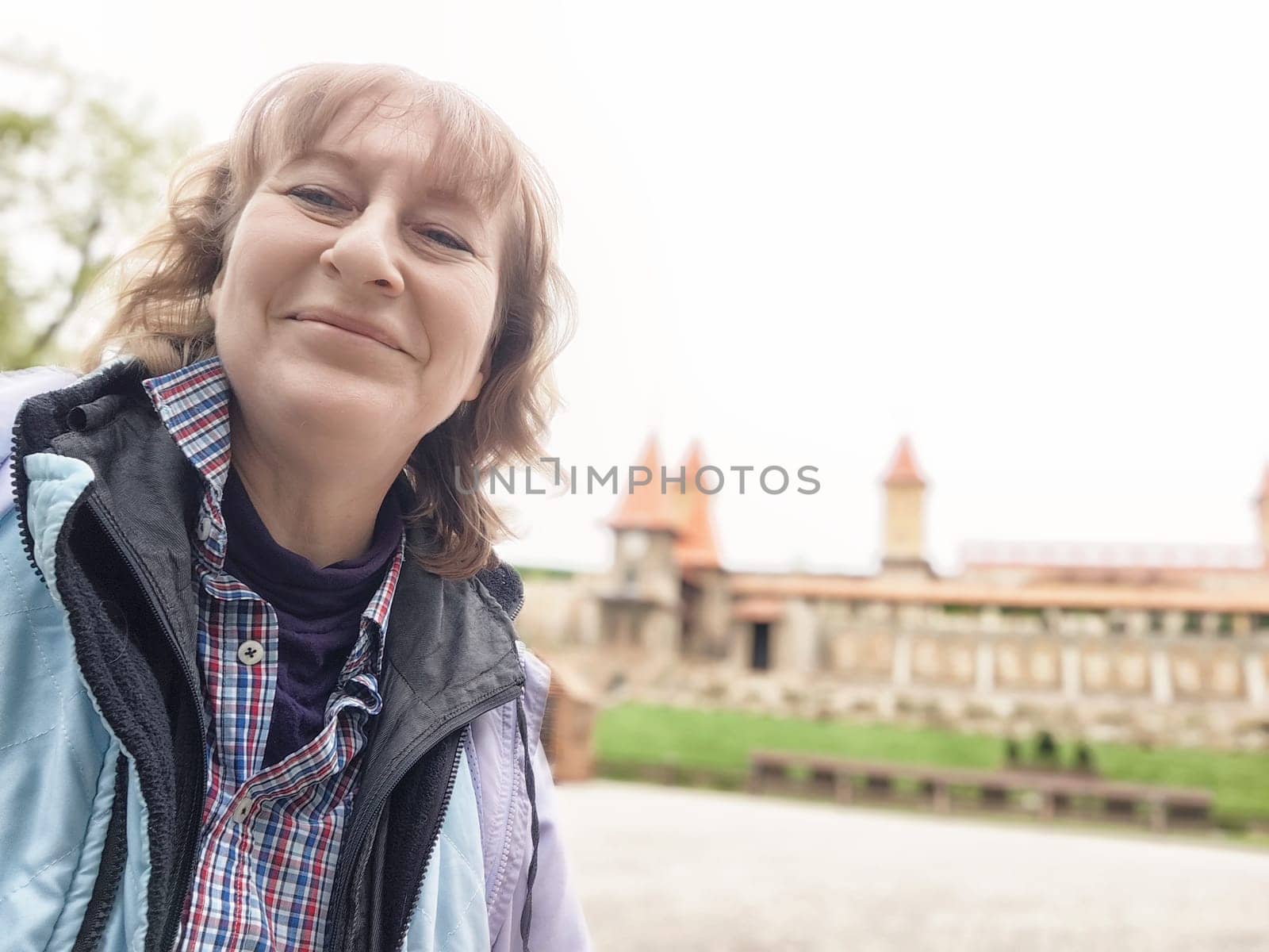 Blonde woman captures joyful selfies in a park while exploring a beautiful landscape during her trip.