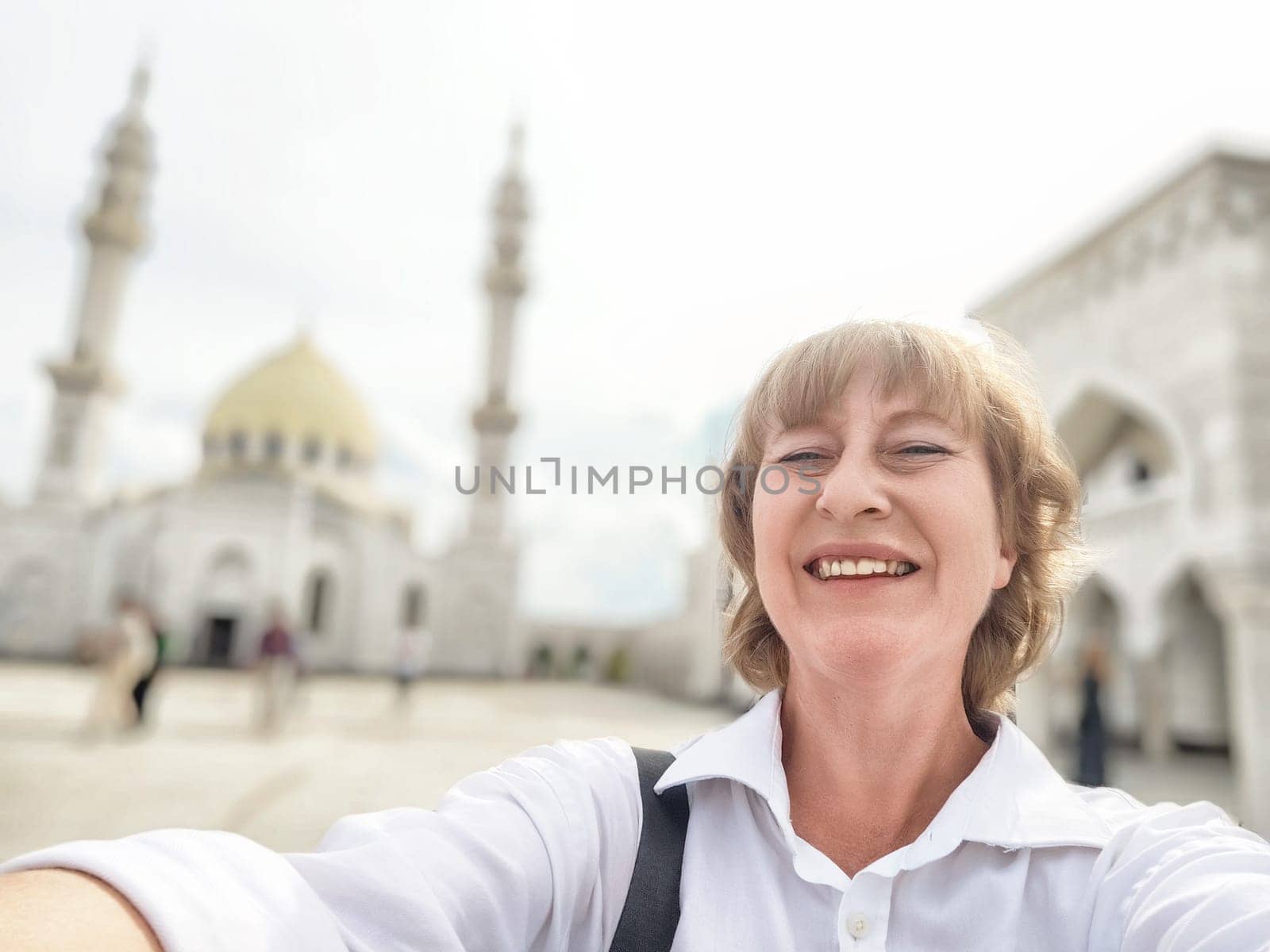 Smiling traveler captures a joyful selfie in front of a beautiful mosque while exploring the area on a sunny day.