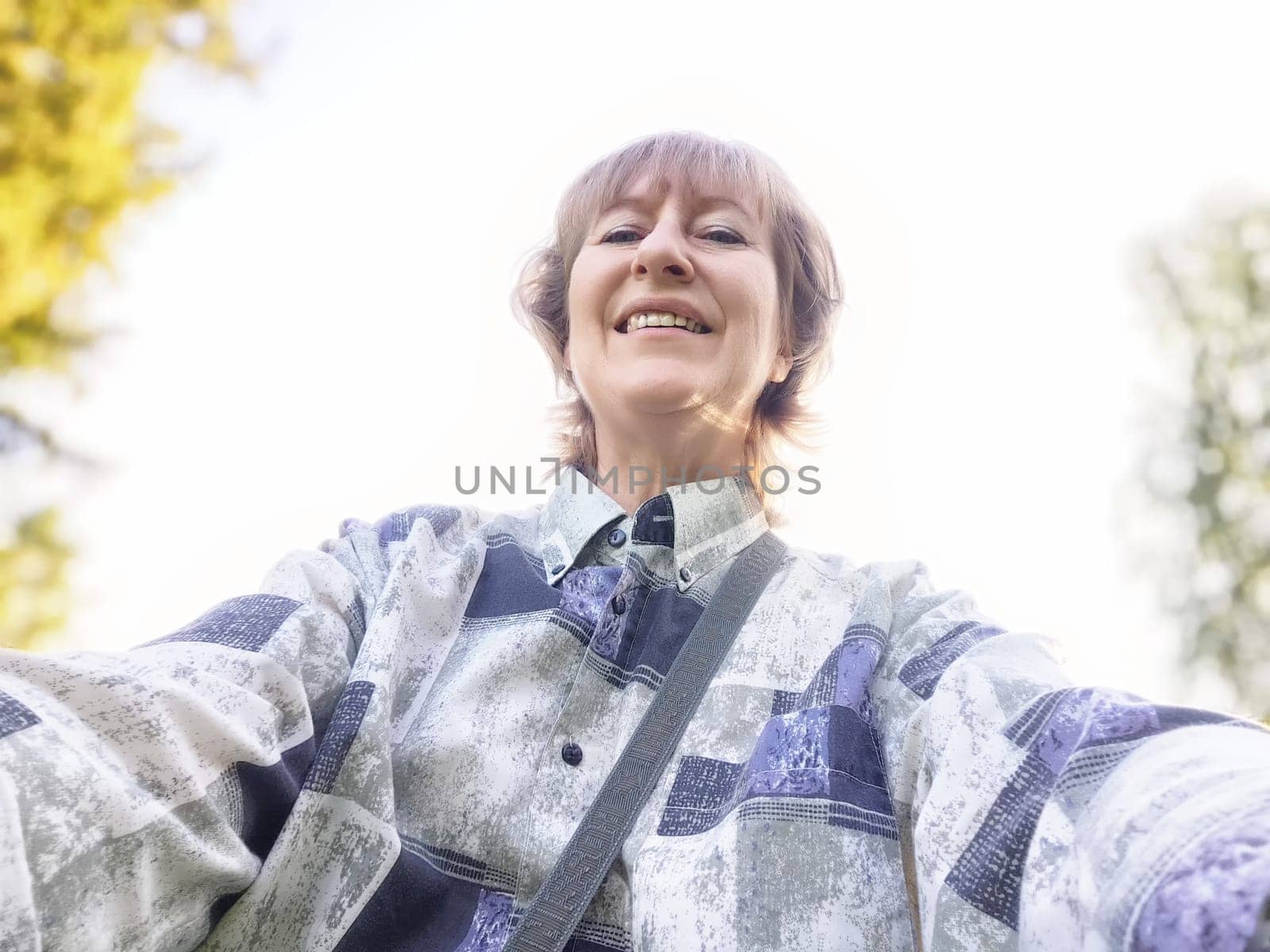 A traveler blogger smiles for a selfie, capturing the joy of her outdoor excursion in a natural setting on a sunny day.