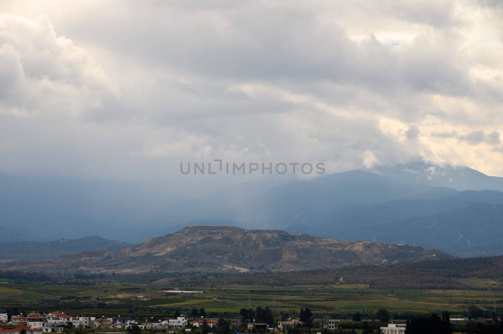 Dark clouds roll over rolling hills and valleys, creating a moody atmosphere in a peaceful rural setting.