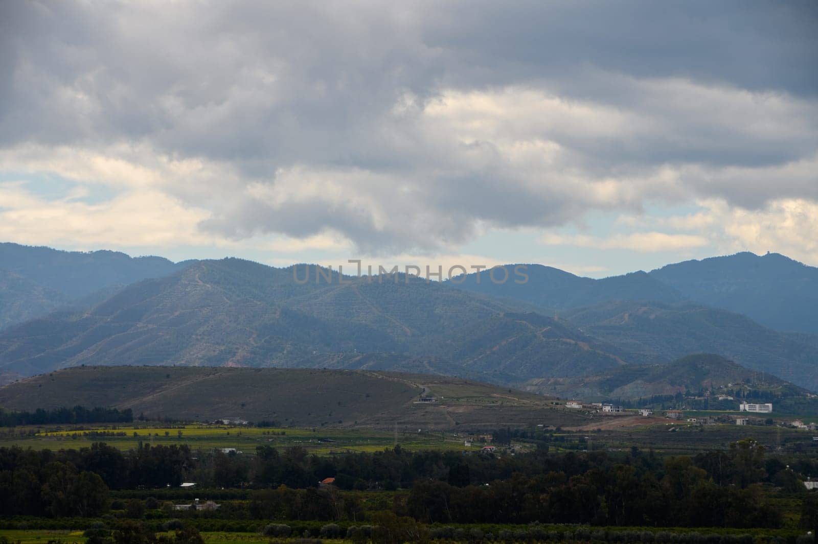 Rolling mountains are beautifully silhouetted against a stormy sky above vibrant greenery in the valley below.