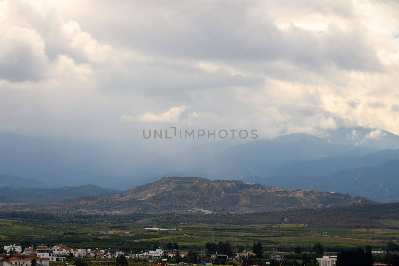 An expansive view reveals rolling mountains, a rustic village, and darkening clouds threatening rain.