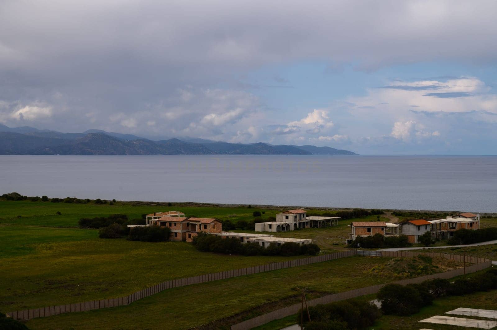 Gentle waves lap against the shore as quaint houses overlook the beautiful expanse of the ocean and distant mountains.