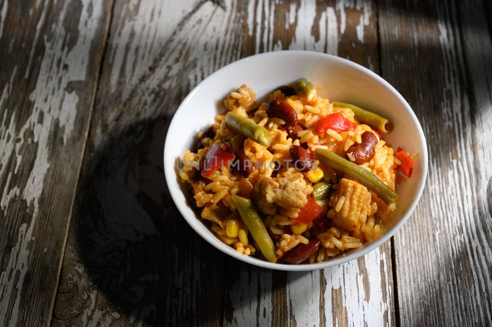 Colorful bowl brimming with rice, beans, and vegetables set on a weathered wooden table, inviting warm flavors.