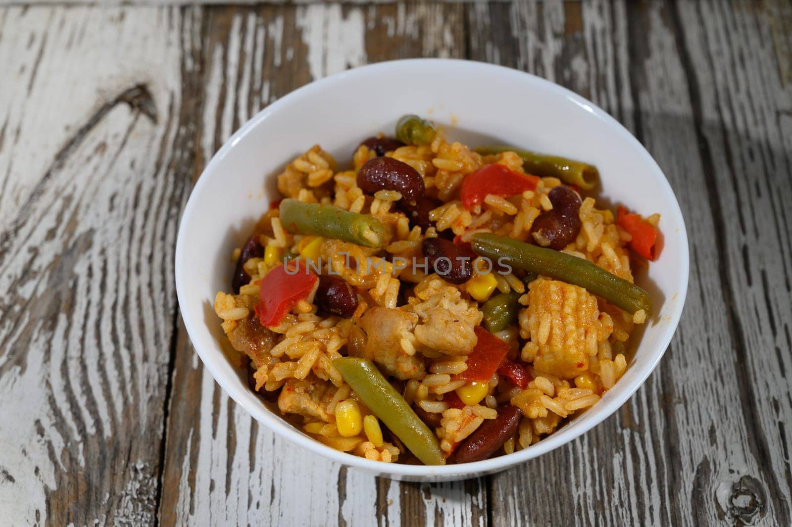 A colorful combination of rice, beans, and fresh vegetables presented in a charming bowl on a weathered wooden table.