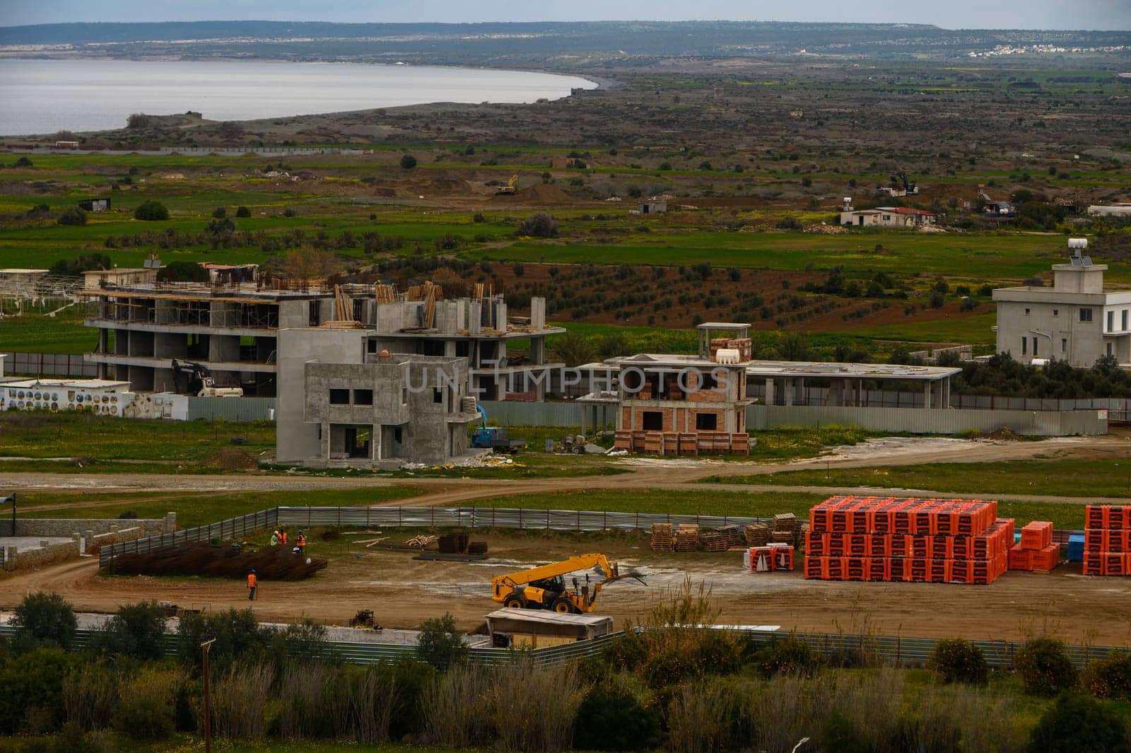 Workers engage in building activities amid scenic views of the coast and lush fields, highlighting local development.