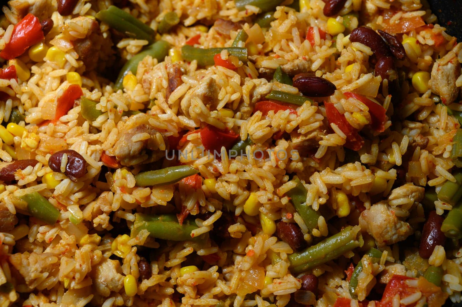 A vibrant mix of rice, chicken, and vegetables is being prepared, emitting an inviting aroma in the cozy kitchen.