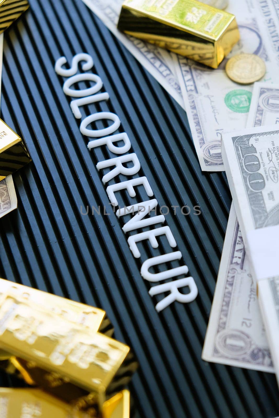 Business concept. Gold bars and dollars on a black background with the word solopreneur.