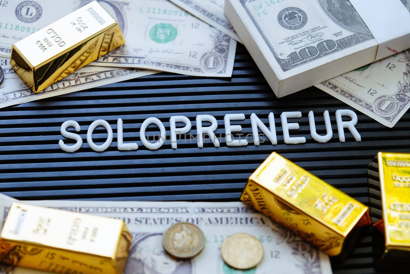 Business concept. Gold bars and dollars on a black background with the word solopreneur.