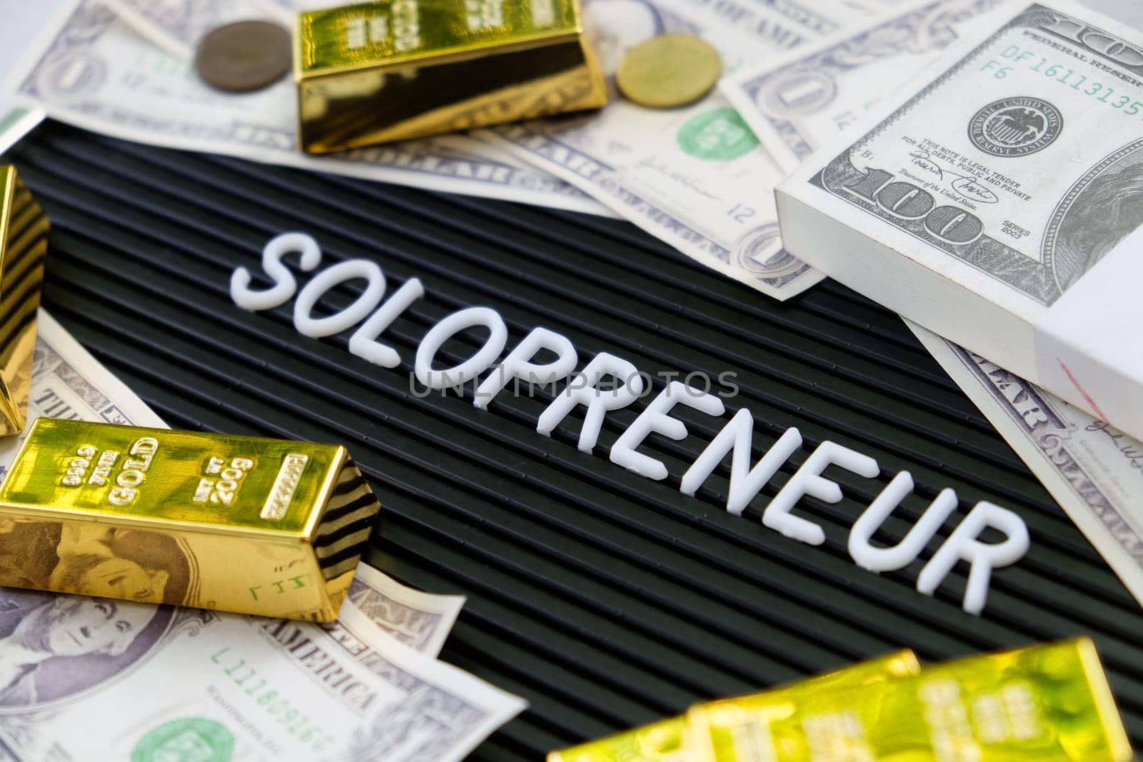 Business concept. Gold bars and dollars on a black background with the word solopreneur.