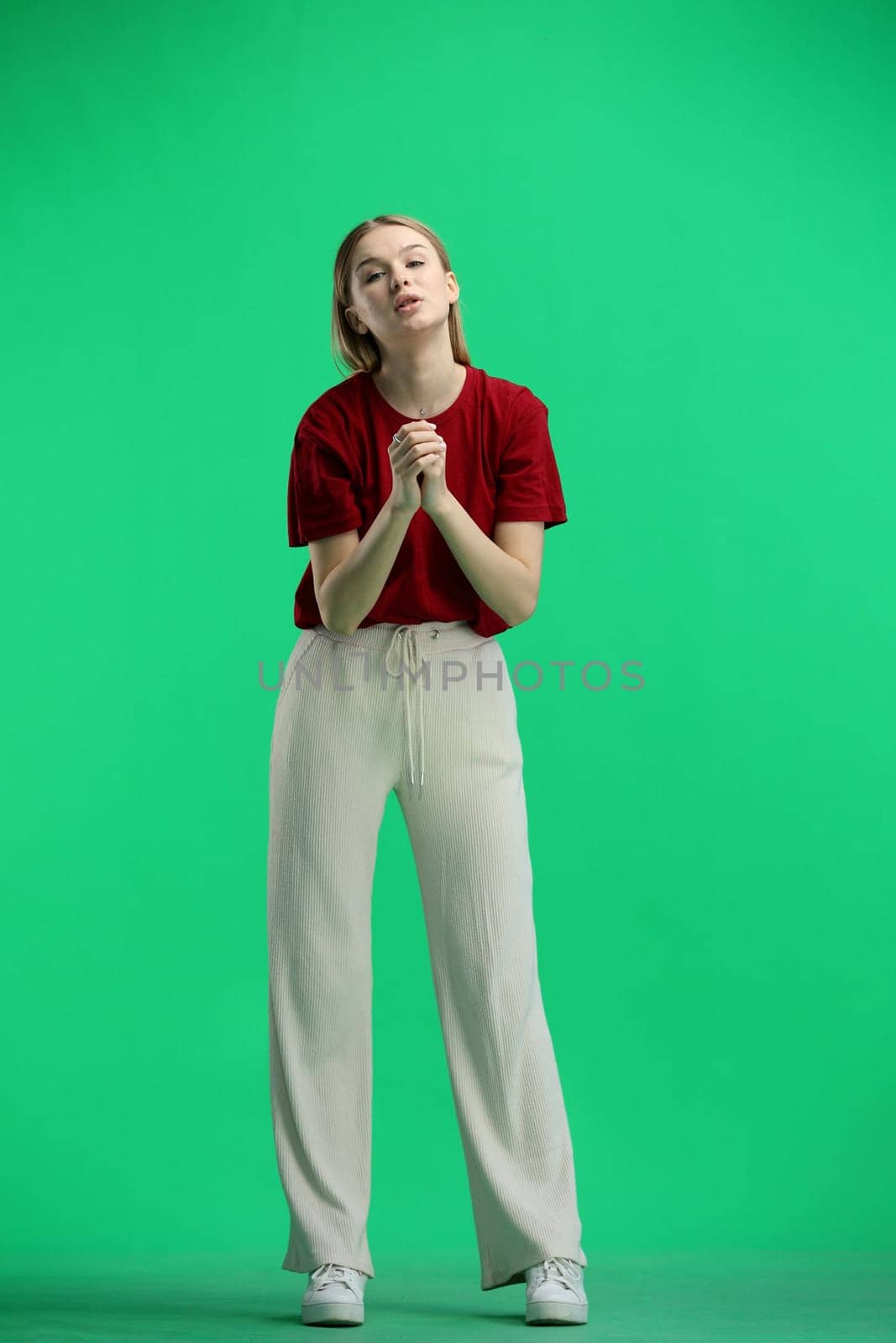 A woman, full-length, on a green background, pleads.
