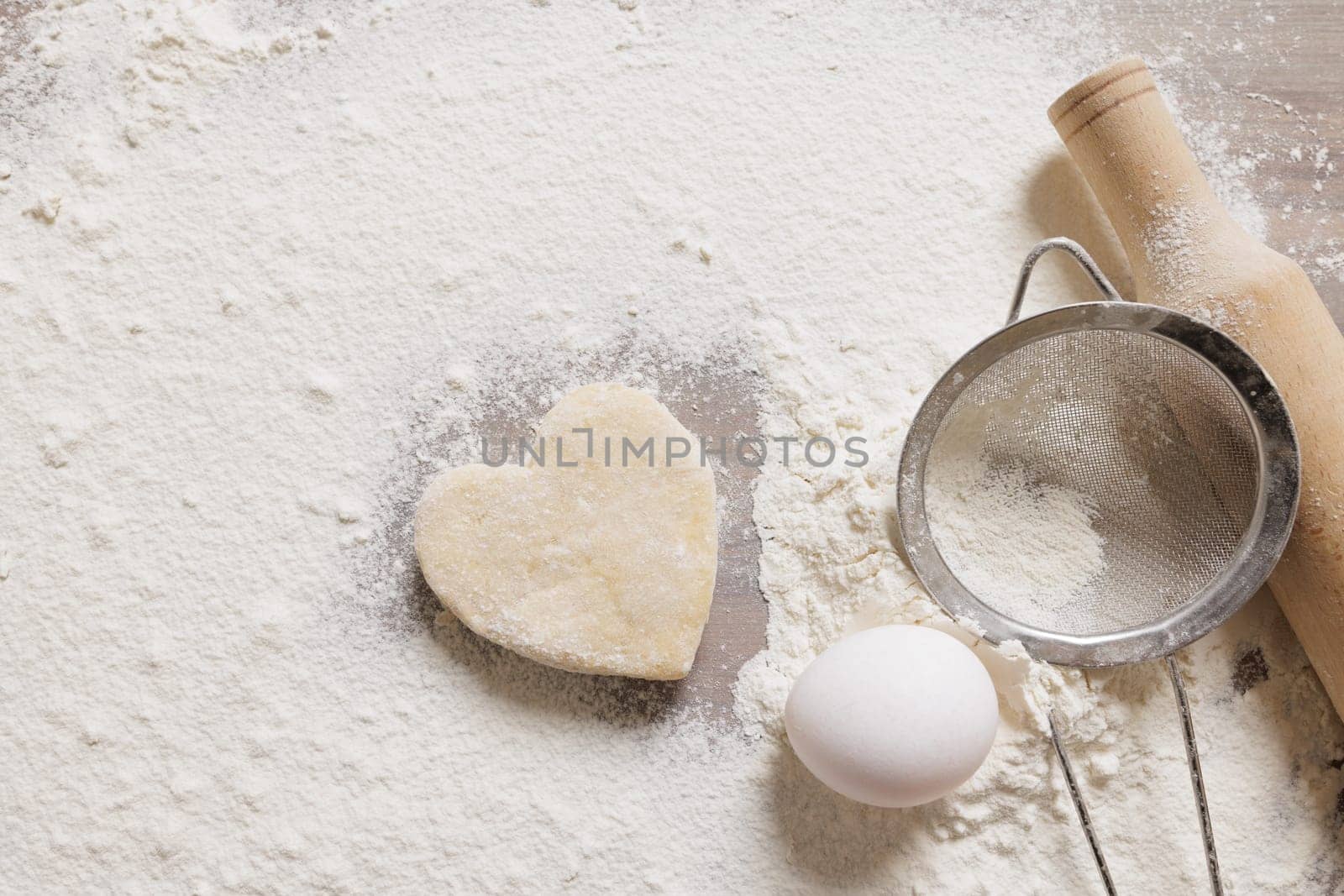 Heart-shaped cookie dough on floured surface with egg, rolling pin, and sieve homemade baking for Valentine's Day or festive culinary concept.