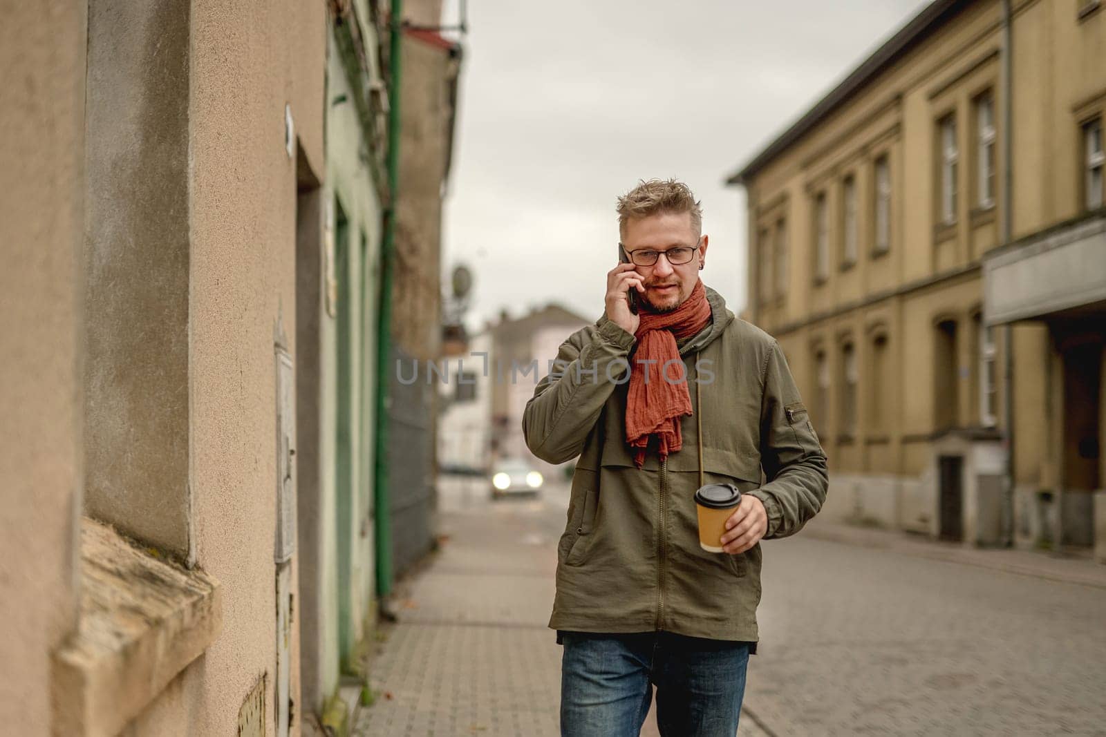 Attractive Stylish Man Walks On The City Street, Talking On The Phone And Drinking Coffee