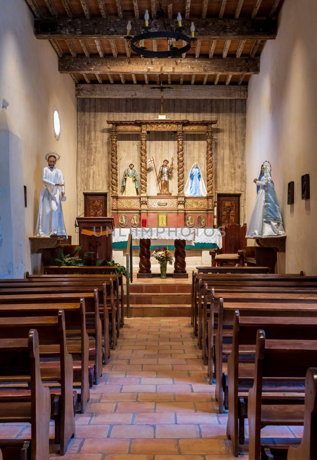 Inside the Mission San Juan church with rows of wooden benches leading to the altar and statues.