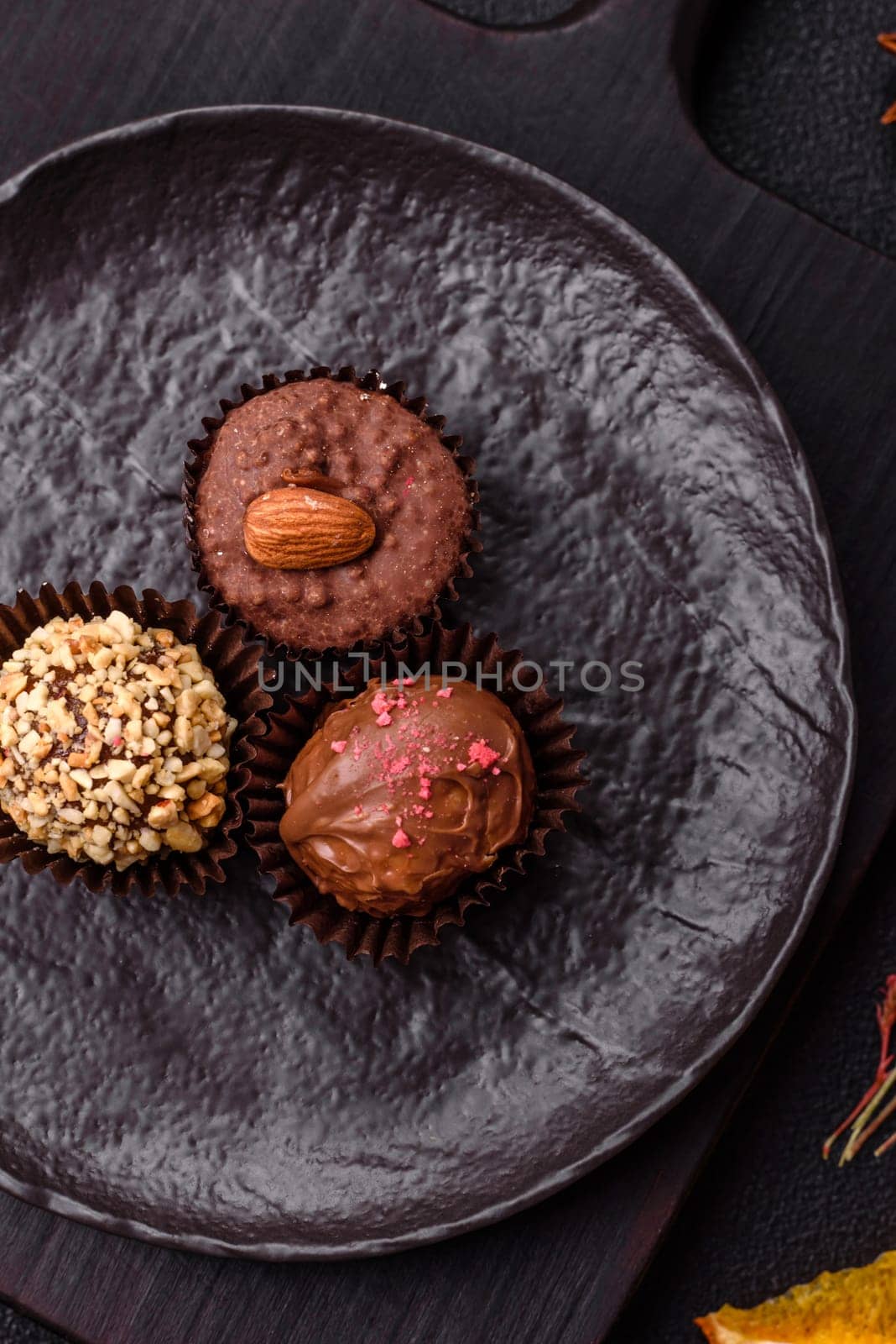 Homemade chocolate candies with different fillings and sprinkles on a dark concrete background