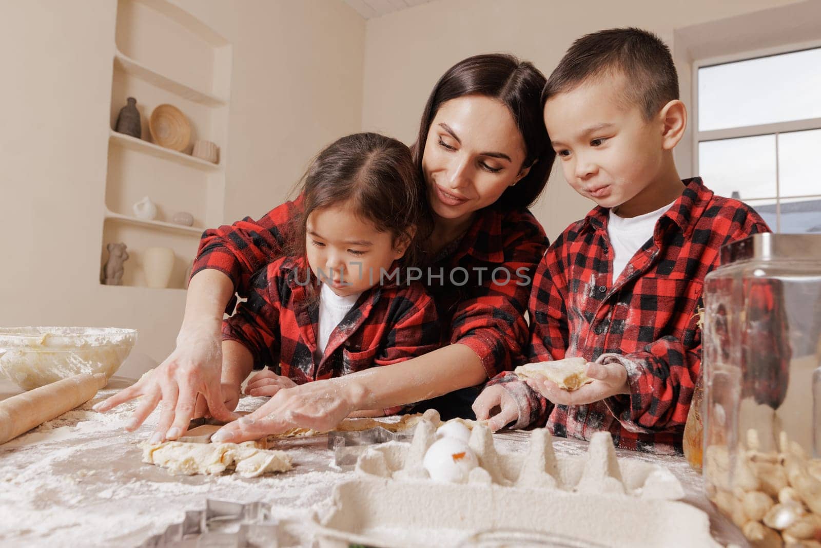 Happy mother and children baking together, family fun in the kitchen, messy hands, playful bonding, homemade cooking, joyful childhood moments.