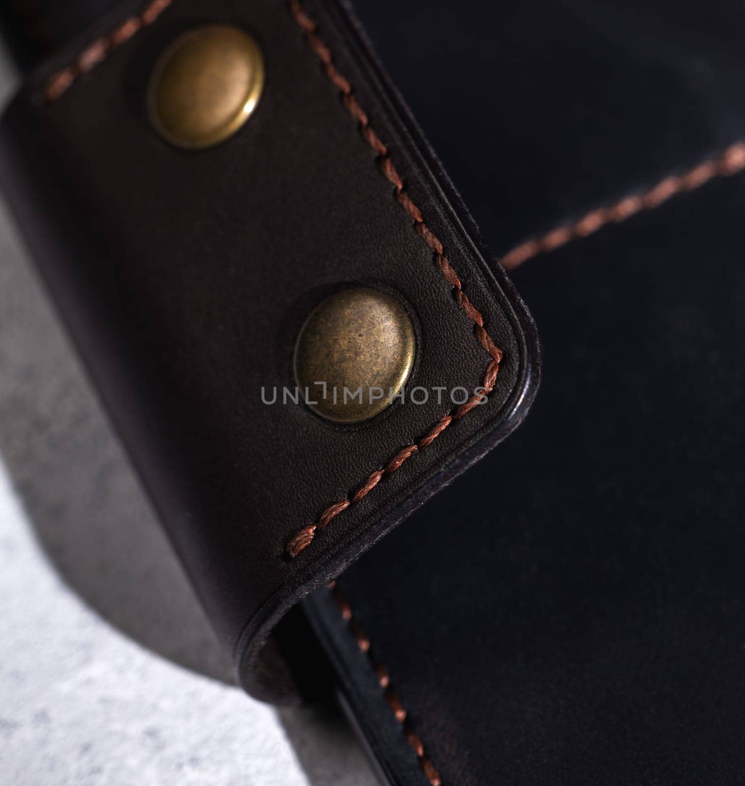 Brown thread stitching detail on dark leather with brass rivets, showcasing craftsmanship