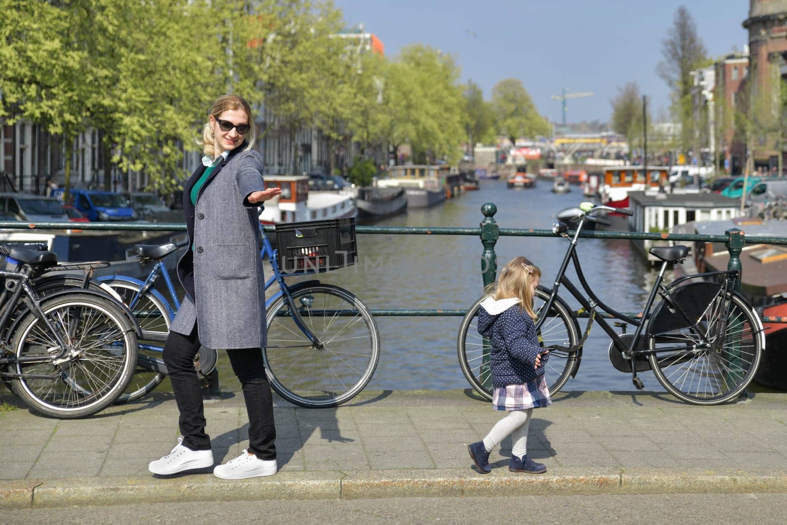 Blonde Dutchwoman mother with her daughter near the bicycle on the bridge over the water channel in Amsterdam city
