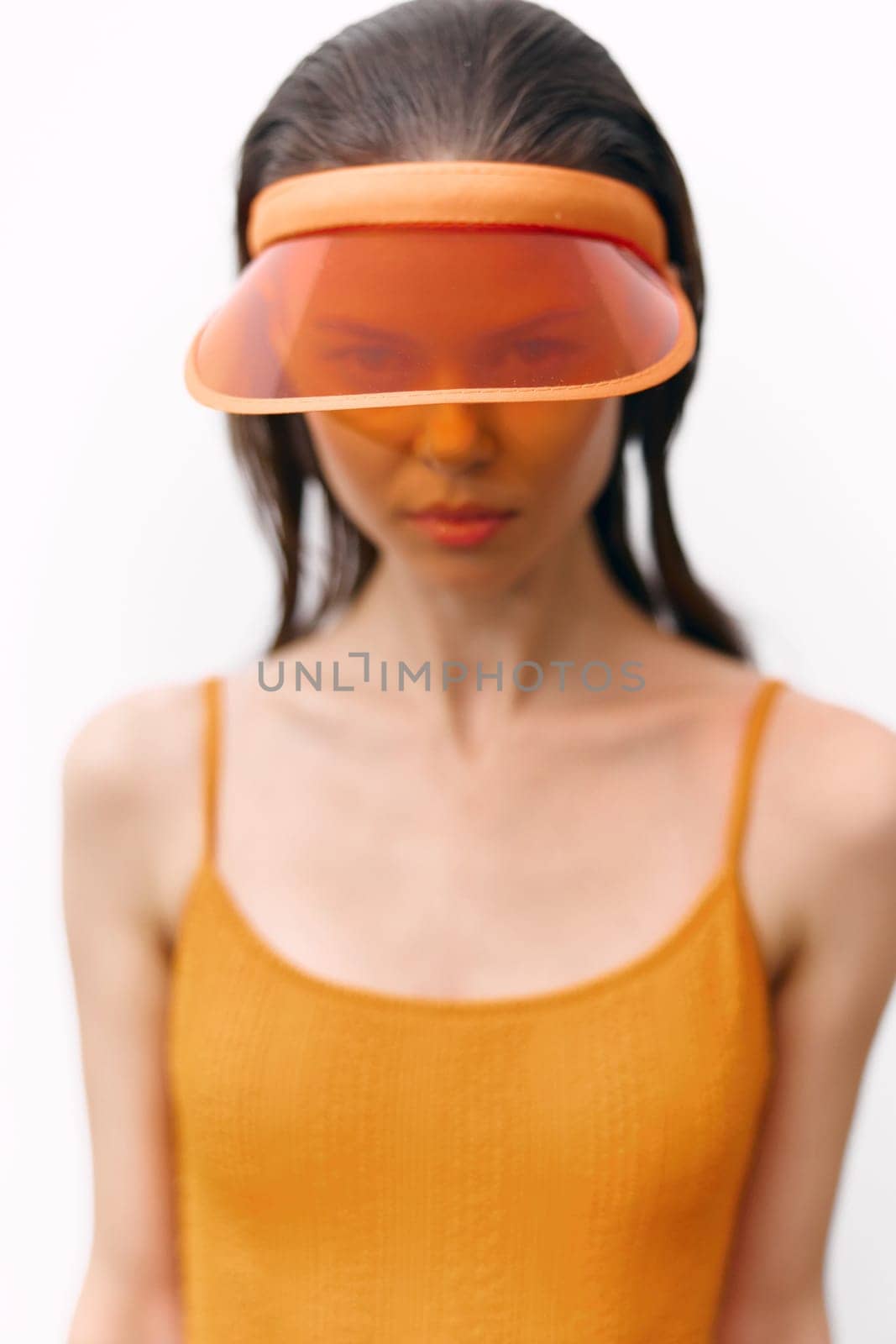 Fashionable female model showcasing a vibrant orange visor and dress against a minimalist white background, perfect for summer-themed editorial content.