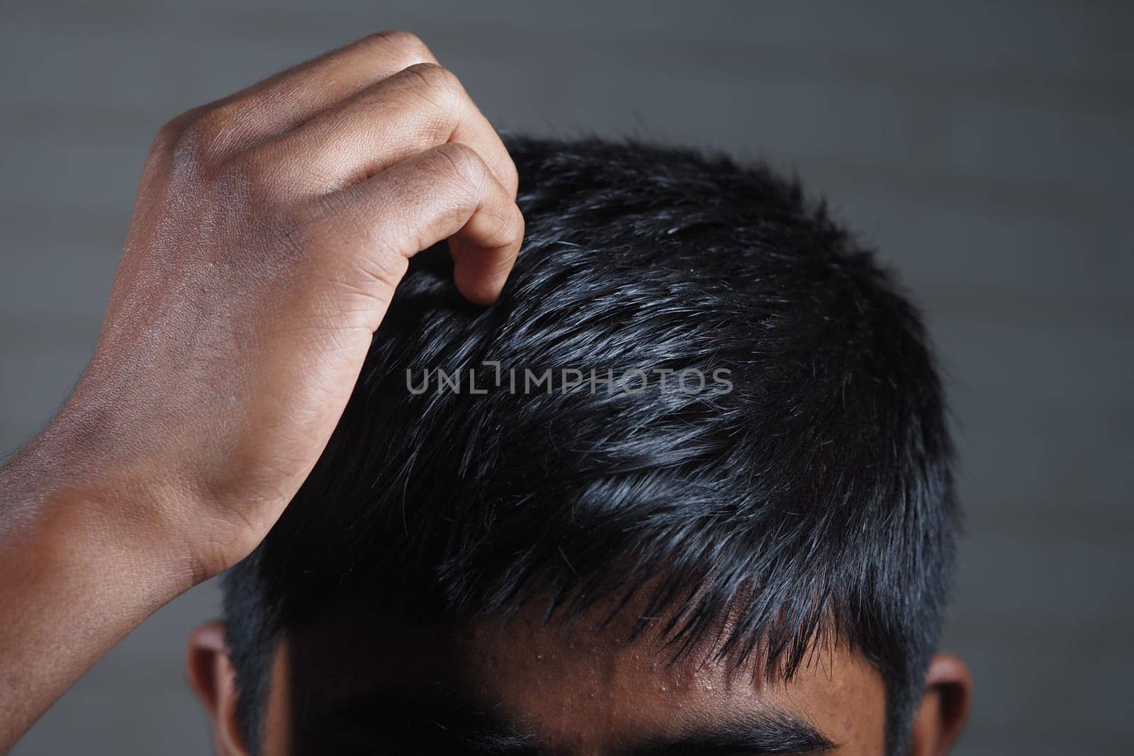 A boy is thinking deeply while scratching his head indoors.