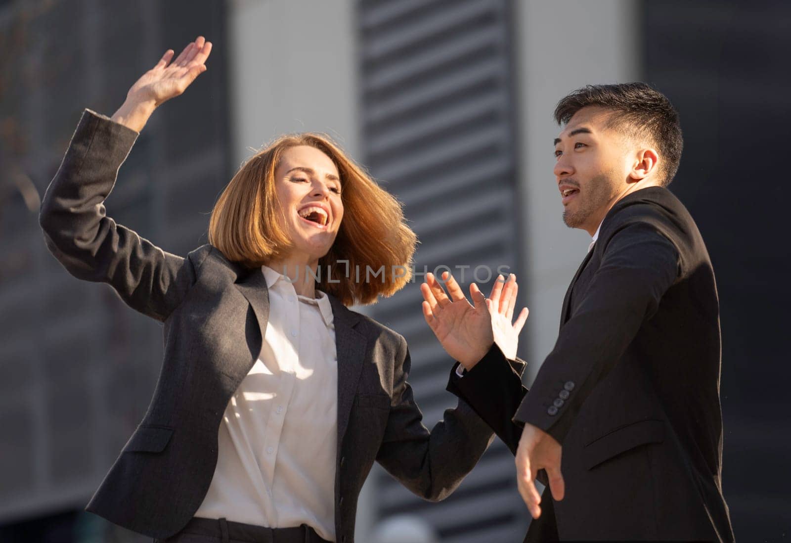 Two business partners celebrating success outdoors, raising their hands in excitement and smiling