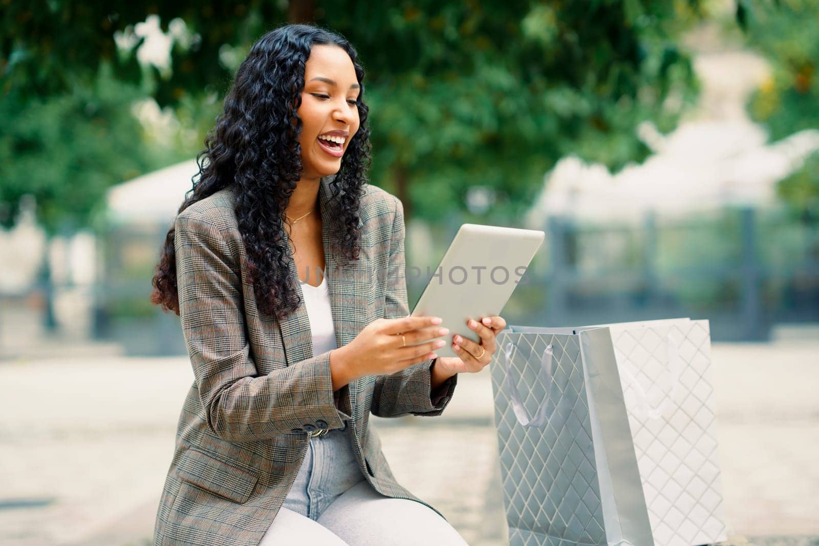A cheerful woman is happily enjoying her tablet in a vibrant green outdoor setting, perfectly showcasing the blend of modern technology and leisurely enjoyment amidst natures beauty