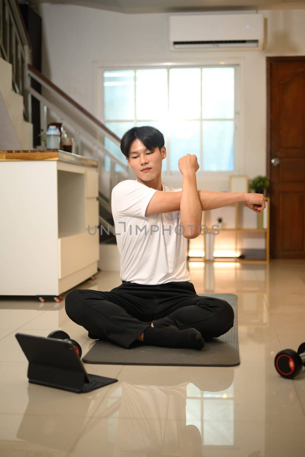 Happy asian man stretching his arms while following an online workout on digital tablet.