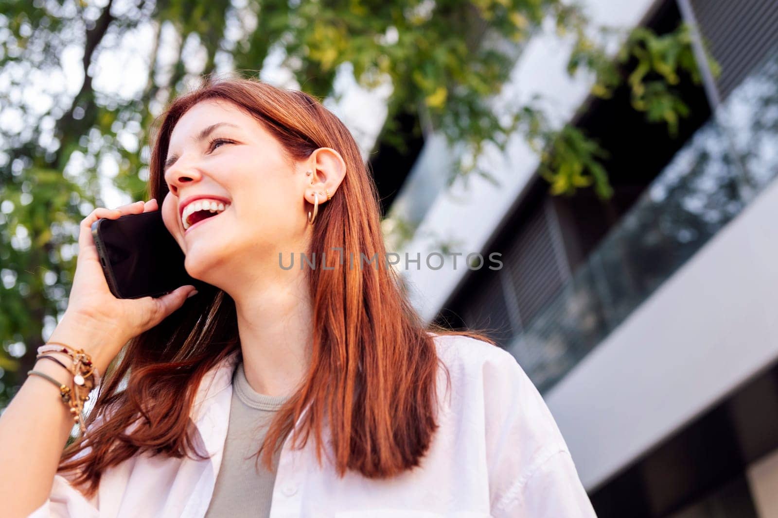 young woman laughing happy while walking down the street in a good mood talking on cell phone, concept of technology of communication and urban lifestyle, copyspace for text