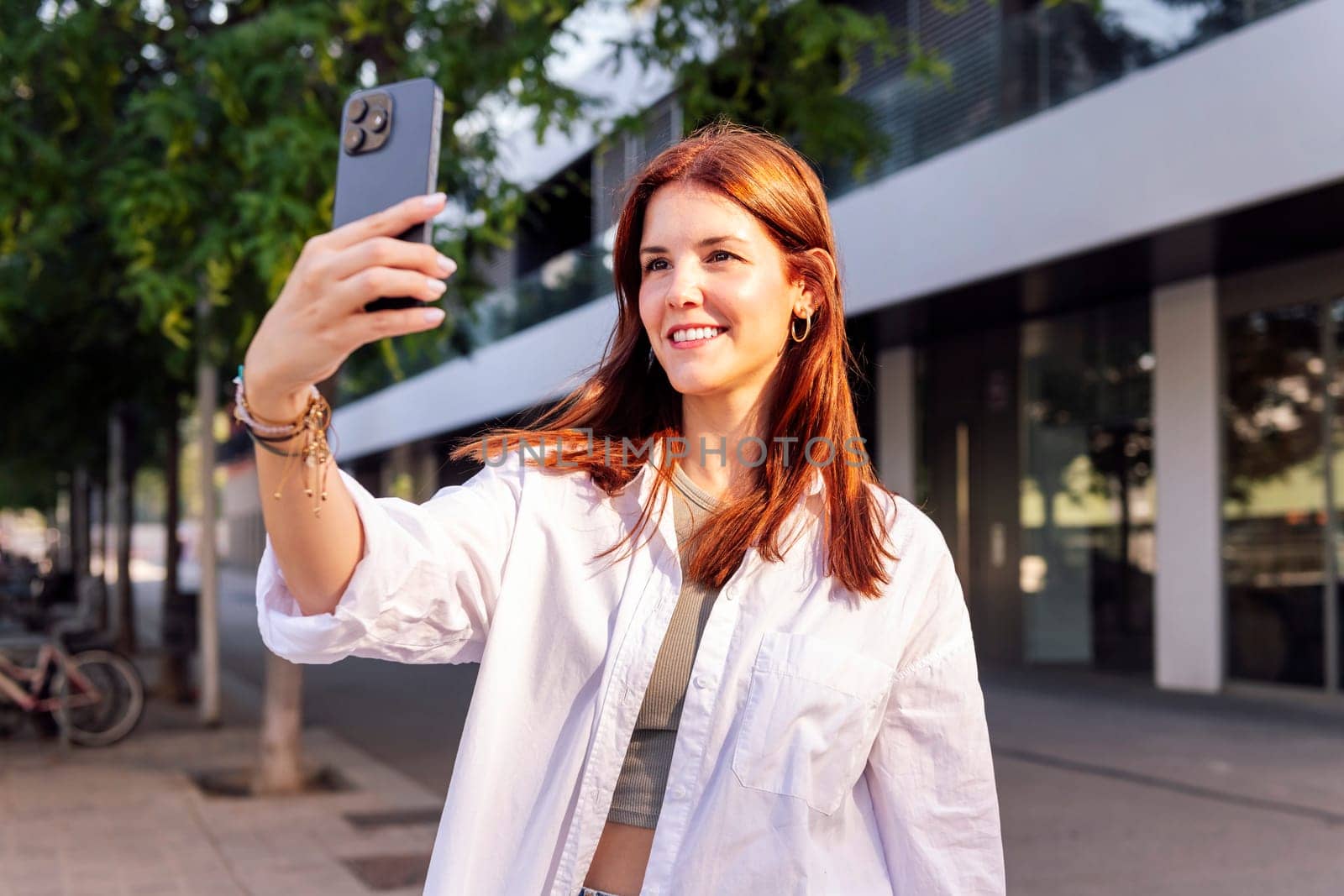 smiling young woman taking a selfie with cell phone, she is happy and enjoying the moment, concept of technology of communication and urban lifestyle