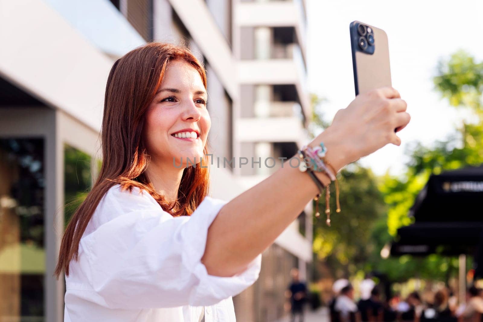 smiling young woman taking a selfie with cell phone, she is happy and enjoying the moment, concept of technology of communication and urban lifestyle