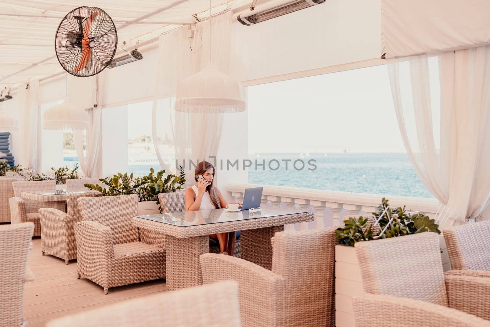Woman coffee cafe laptop sea. Female freelancer using laptop on coffee break in modern cafe with sea view in the morning.