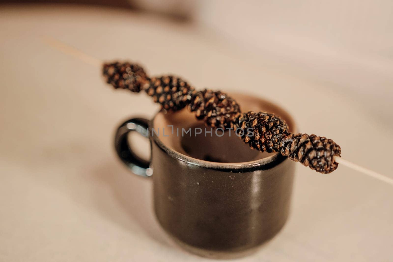 Dark brown coffee in a small mug. A thin skewer with dark brown, spiraled adornments rests across the top. Close-up view on a light beige surface.